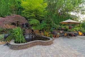 Backyard garden landscaping with waterfall and pond with hardscaping.