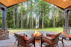 Large backyard, two chairs around a firepit on hardscape looking at the woods.